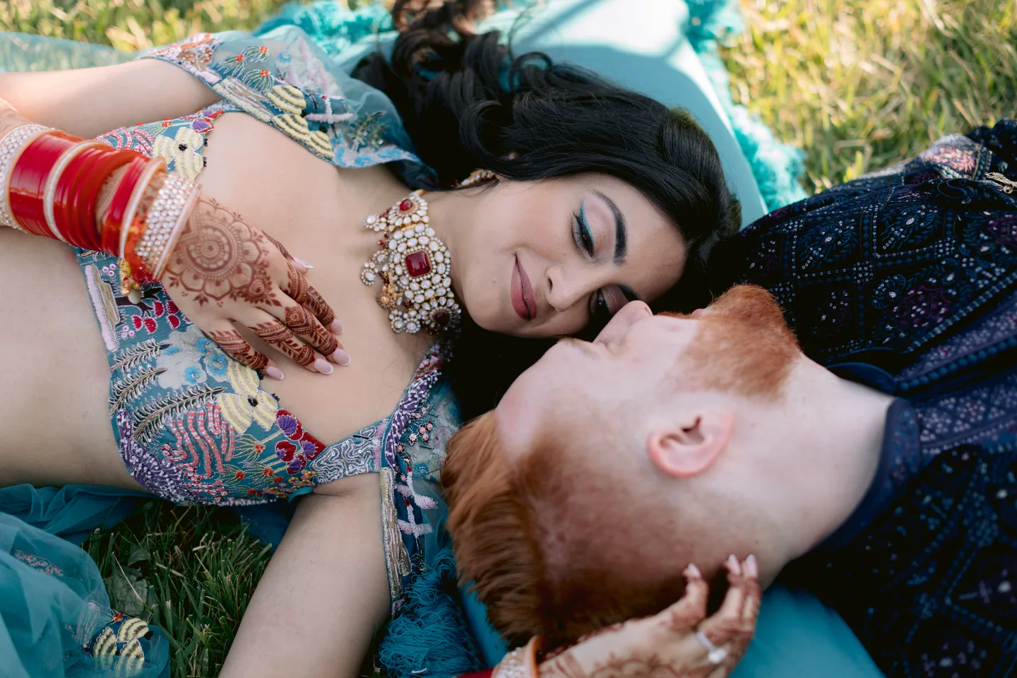 Reena and Zach resting together on the grass in colorful Sangeet attire